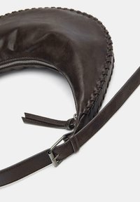 Brun læder skuldertaske med et buet design, fletninger langs kanten og en justerbar rem med metalhardware.
