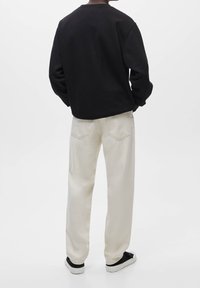 Czarna bluza z długimi rękawami i okrągłym dekoltem, w połączeniu z jasnobeżowymi spodniami o luźnym kroju i subtelnymi detalami w postaci kieszeni z tyłu.