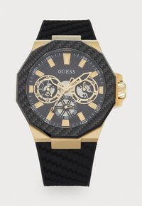 Orologio con cinturino in gomma nera e dettagli oro, cassa ottagonale, quadrante nero testurizzato, tre subquadranti e marcatori delle ore pronunciati. Lancette del quadrante in argento.