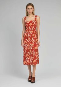 Robe maxi rouge à fleurs avec encolure carrée et larges bretelles. Présente une taille ajustée, une jupe fluide et une fente sur le côté. Talons plateformes marron inclus.