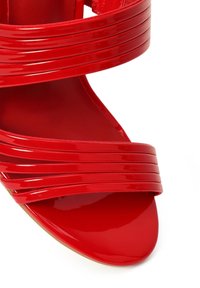 Sandalia roja de charol con punta abierta y tres tiras horizontales sobre el dedo y el tobillo.