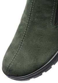 Nahaufnahme des vorderen Teils eines grünen Wildlederschuhs mit sichtbaren Nähten und einer schwarzen Gummisohle.