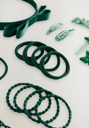 Accesorios para el cabello verdes dispuestos sobre una superficie blanca: una diadema de cinta, múltiples gomas para el cabello y horquillas con estampados.
