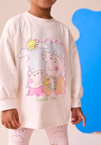 Cream sweatshirt featuring a cartoon design of pigs, sun, and clouds. Paired with light pink leggings decorated with clouds. Soft fabric.