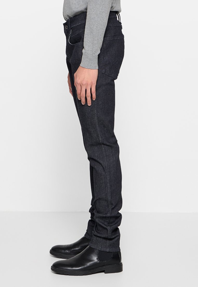 Dunkelblaue Jeans im Slim-Fit-Schnitt, mit einem klassischen Fünf-Taschen-Design, dezenten Nähten und einer glatten Textur, kombiniert mit schwarzen Knöchelstiefeln.