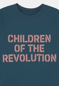 Sweatshirt verde-escuro com decote redondo. Apresenta texto rosa em negrito a dizer "FILHOS DA REVOLUÇÃO." Tecido macio e texturizado.