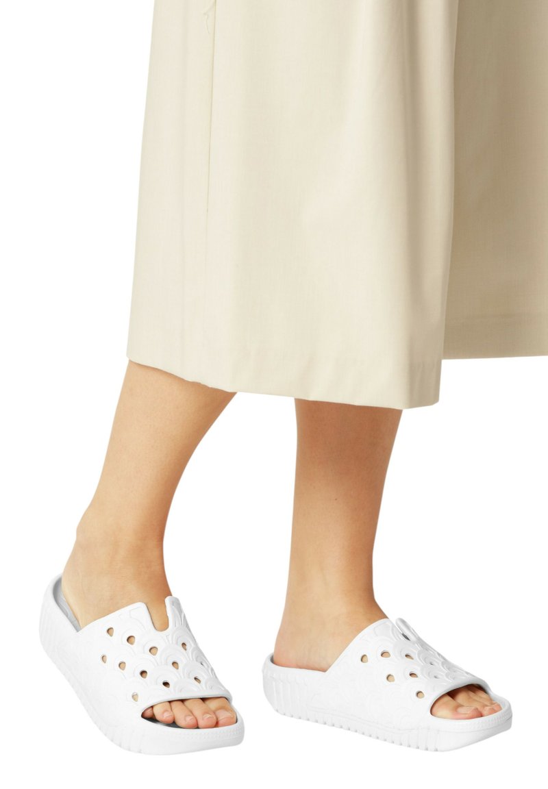 Zoccoli bianchi slip-on con fori intagliati, tomaia testurizzata e una suola spessa con scanalature. Presentano un design morbido e flessibile per il massimo comfort.