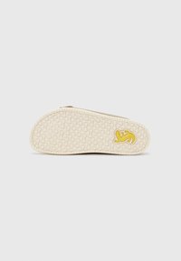 Shoe sole with textured rubber material in cream color; features a yellow logo and patterned tread for traction.