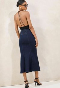 Denim midi šaty s čiernou korzetovou časťou, otvoreným chrbtom, nastaviteľnými ramienkami, postrannými rozparkami a obopnutým pásom. Lesklé čierne lodičky na vysokom opätku.