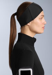 Bandă sportivă neagră din material elastic, cu o suprafață netedă și o potrivire confortabilă, purtată cu un top negru cu fermoar asortat.