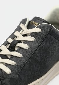 Μαύρο sneaker από δερματίνη με υφή, με εκρού κορδόνια, μαύρο σιδεράκι κορδονιών και χρυσή λεπτομέρεια λογότυπου στη γλώσσα. Λείο καουτσούκ πέλμα.