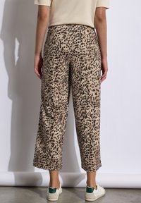 Imprimé léopard, pantalons beiges à coupe ample ; jambes raccourcies et taille élastique ; tissu lisse et léger éclat ; associés à des chaussures blanches.