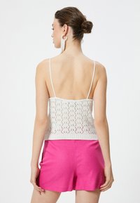 Top sin mangas de punto blanco con diseño de calado, combinado con pantalones cortos rosas brillantes. Presenta tirantes finos y un estilo recortado.