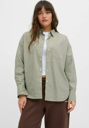 Green and white striped button-up shirt with a collar, long sleeves, and a chest pocket, paired with brown sweatpants.