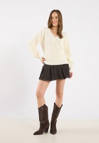 Ivory ribbed knit sweater with a V-neck, paired with a dark denim skirt featuring a frayed hem, and brown embroidered cowboy boots.
