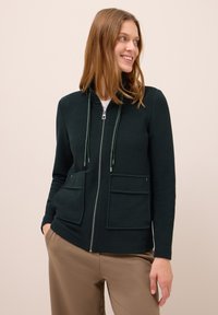 Tmavě zelená zipová mikina s texturovanou tkaninou, vyznačující se vysokým límcem, dvěma předními kapsami a šňůrkami s kovovými konci.