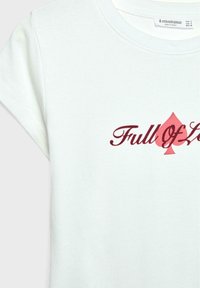 T-shirt en coton vert clair arborant un graphique "Plein d'Amour" en rouge foncé, orné d'une forme de pique rouge au-dessus du texte.