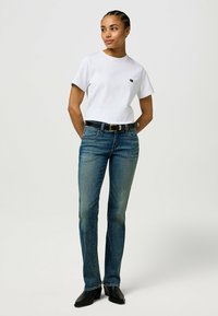 Hvid bomulds t-shirt med et lille sort logo, parret med falmede blå lige ben jeans og et sort læderbælte, båret med sorte ankelstøvler.