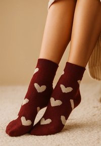 Bordeauxrote Socken mit einem wiederholten Muster aus weißen Herzen, gestrickter Textur, knöchelhohem Design und gerippten Bündchen. Gemütliche und lässige Trageweise.