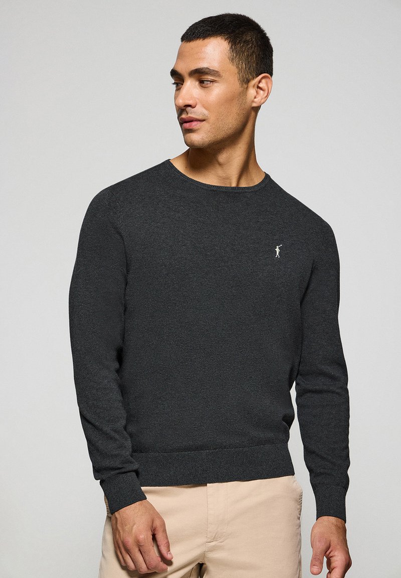 Suéter de punto gris oscuro con cuello redondo, puños y dobladillo acanalados. Presenta un pequeño logo blanco en el lado izquierdo del pecho. Textura suave.