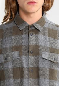 Flanellhemd im grau-olivgrünen Karomuster, mit klassischem Kragen, durchgehender Knopfleiste und aufgesetzten Brusttaschen. Weiche Textur.