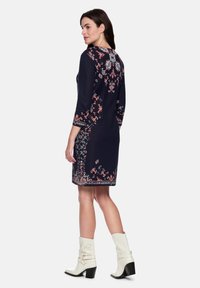 Marineblaues Kleid mit aufwendiger Blumstickerei in Rot und Weiß, dreiviertellangen Ärmeln, rundem Ausschnitt und figurbetonter Silhouette.