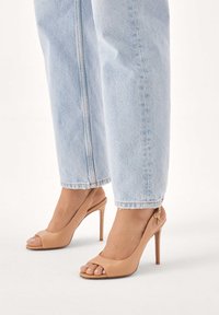 Beżowe sandały na wysokim obcasie z odkrytymi palcami i tylnym paskiem wokół pięty. Gładka skóra z małym złotym akcentem na obcasie.