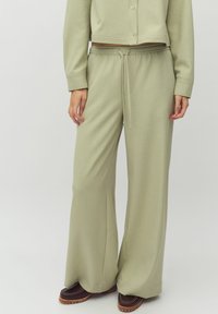 Lichtgroene, brede broek gemaakt van zacht materiaal, met een koord taille en een gladde textuur. Gecombineerd met donkerbruine schoenen.