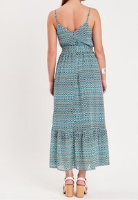 Robe longue avec un motif géométrique bleu-vert, bretelles spaghetti réglables, taille cintrée et ourlet à volants à étages. Talons blocs en bois.