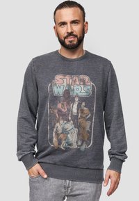 Felpa grigia con una grafica vintage di "Star Wars" che presenta personaggi in vari colori. Polsi e orlo a coste, scollatura rotonda, vestibilità casual.