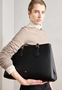 Borsa a tracolla nera in pelle con superficie testurizzata, due manici corti e dettagli in hardware dorato. Presenta una forma triangolare moderna e un branding minimale.