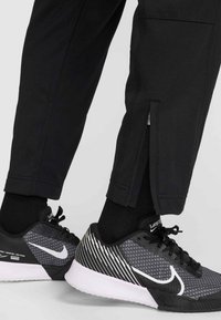 Μαύρο αθλητικό παντελόνι με φερμουάρ στο άνοιγμα των αστραγάλων, σε συνδυασμό με μαύρα και γκρι παπούτσια με υφασμάτινο σχέδιο και λευκές λεπτομέρειες.