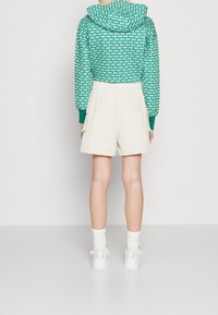 Green patterned cropped hoodie with a drawstring hood, paired with cream shorts and white sneakers, visible from the back.