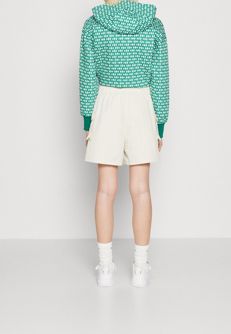 Green patterned cropped hoodie with a drawstring hood, paired with cream shorts and white sneakers, visible from the back.