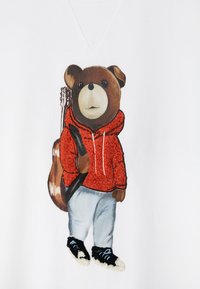 Pamut pulóver, amelyen egy hímzett medve látható piros kapucnis felsőben, szürke nadrágban és fekete cipőben, kezében gitárral, fehér háttéren.