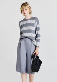 Maglione a righe grigio e bianco in maglia abbinato a pantaloni palazzo grigio chiaro. Il modello tiene una piccola borsa in pelle nera, presenta una vestibilità rilassata e una texture a coste.