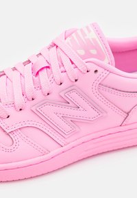 Rosa sportskor med en slät syntetisk ovandel, tonad sömnad, runda snörning och en texturerad logotypdekoration på sidan.