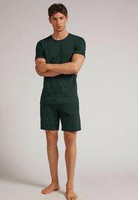 Grünes Baumwoll-T-Shirt mit kurzen Ärmeln und passenden Shorts. Der Stoff wirkt glatt und hat eine lockere Passform. Keine sichtbaren Muster oder Verzierungen.