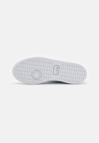 Hvit sneaker såle med rutenettmønster, sirkulært detalj nær fronten, og Lacoste-logoet preget i sentrum.