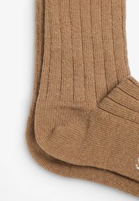 Calcetines de algodón marrón con una textura acanalada y talón reforzado. El diseño incluye un patrón sutil y un acabado suave.