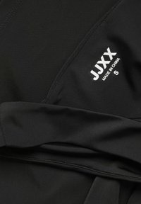 Fekete sportöltözet anyag sima tapintással. Fehér szöveggel rendelkezik: "JUXX MADE IN CHINA S." Rétegezett részekkel és tiszta varrással lett tervezve.