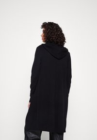 Czarny kardigan z kapturem i długimi rękawami, wykonany z miękkiego materiału. Posiada boczne kieszenie i luźny krój, sięgający do połowy uda.