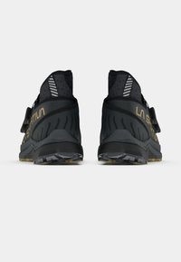 Czarne buty sportowe z wysoką cholewką, odblaskowymi akcentami, teksturowanymi nakładkami oraz złotym logo na pięcie, z solidną podeszwą.