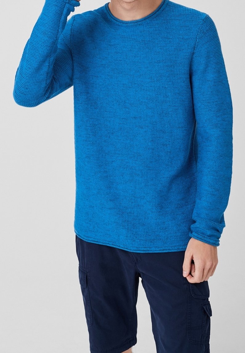 Homme portant une chemise à manches longues bleue texturée et un short cargo bleu marine, une main levée près de sa tête.