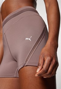 Gros plan sur une personne portant un short de sport mauve avec des détails en mesh et un logo Puma blanc sur la cuisse.