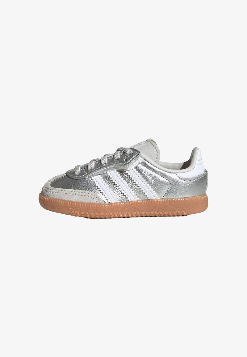 Sølv- og hvide lavtop-sneakers med gummisål, hvide snørebånd, tre hvide striber og teksten "SAMBA" på siden.