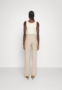 Pantalon beige taille haute avec une coupe droite, associé à un débardeur ajusté couleur blanc cassé. Texture lisse et détails minimalistes visibles.