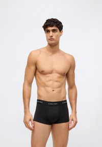 Černé bavlněné boxerky s elastickým pasem s logem "Calvin Klein" v bílé barvě. Model pózuje v neutrální pozici bez trička.