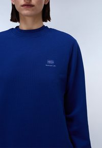 Koninklijk blauwe sweatshirt gemaakt van zacht materiaal, met een ronde hals, lange mouwen en een geborduurd logo op de borst.
