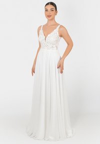 Abito bianco con un corpetto aderente decorato con pizzo floreale e una profonda scollatura a V. Gonna fluida a A realizzata in tessuto morbido.